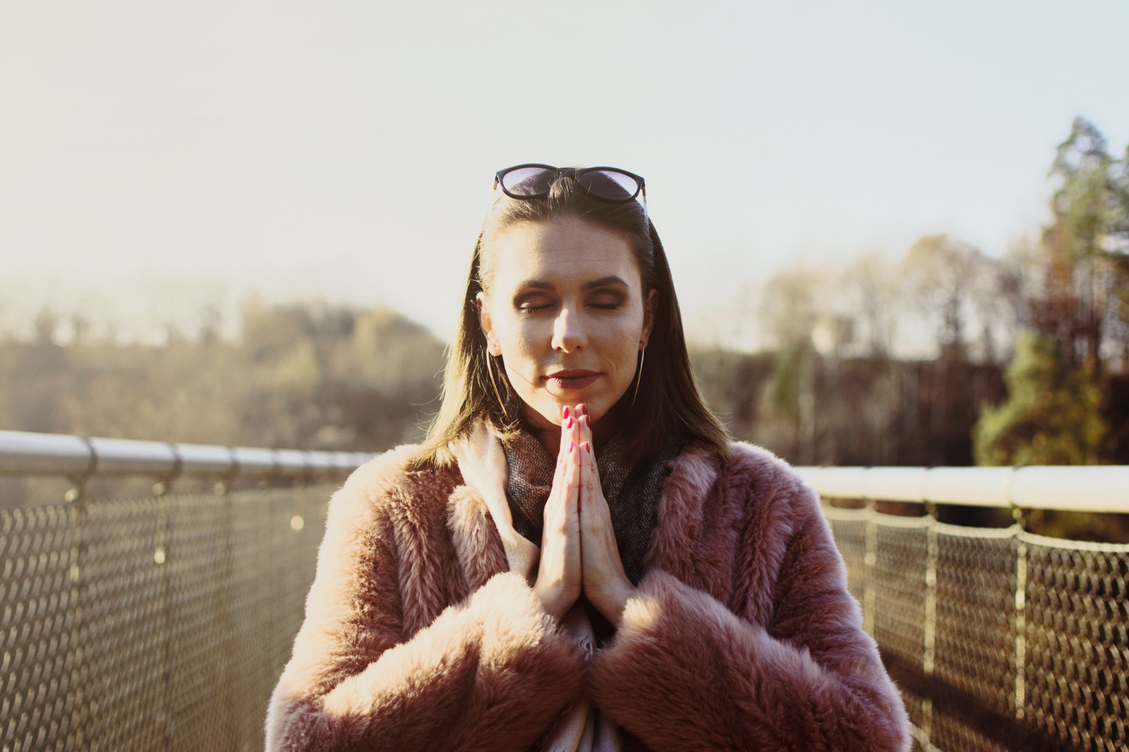 A woman standing outdoors with her eyes closed and palms pressed together at her chest