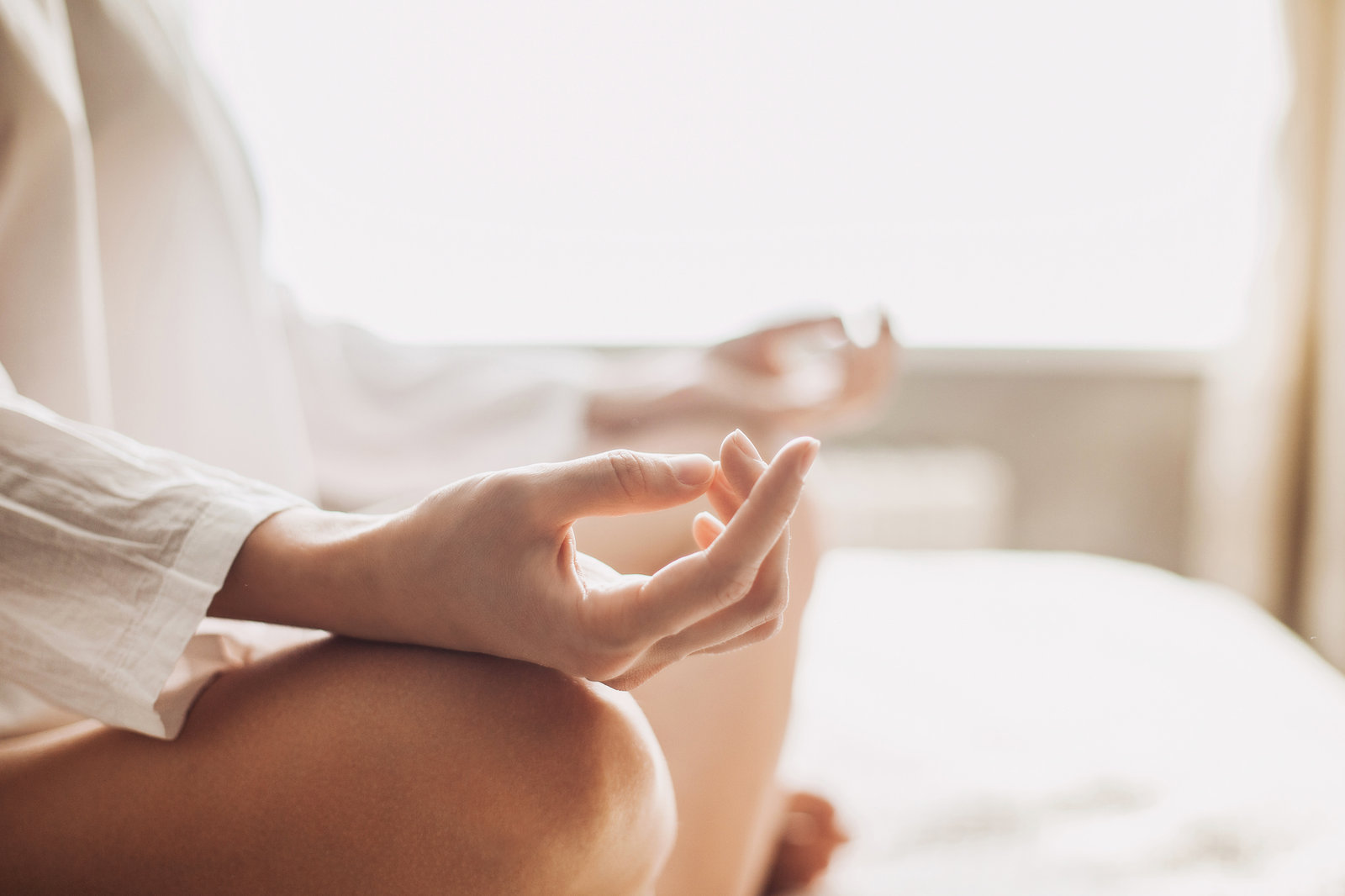Close-up of a person's hands resting on their knees in a meditation posture, in bright daylight