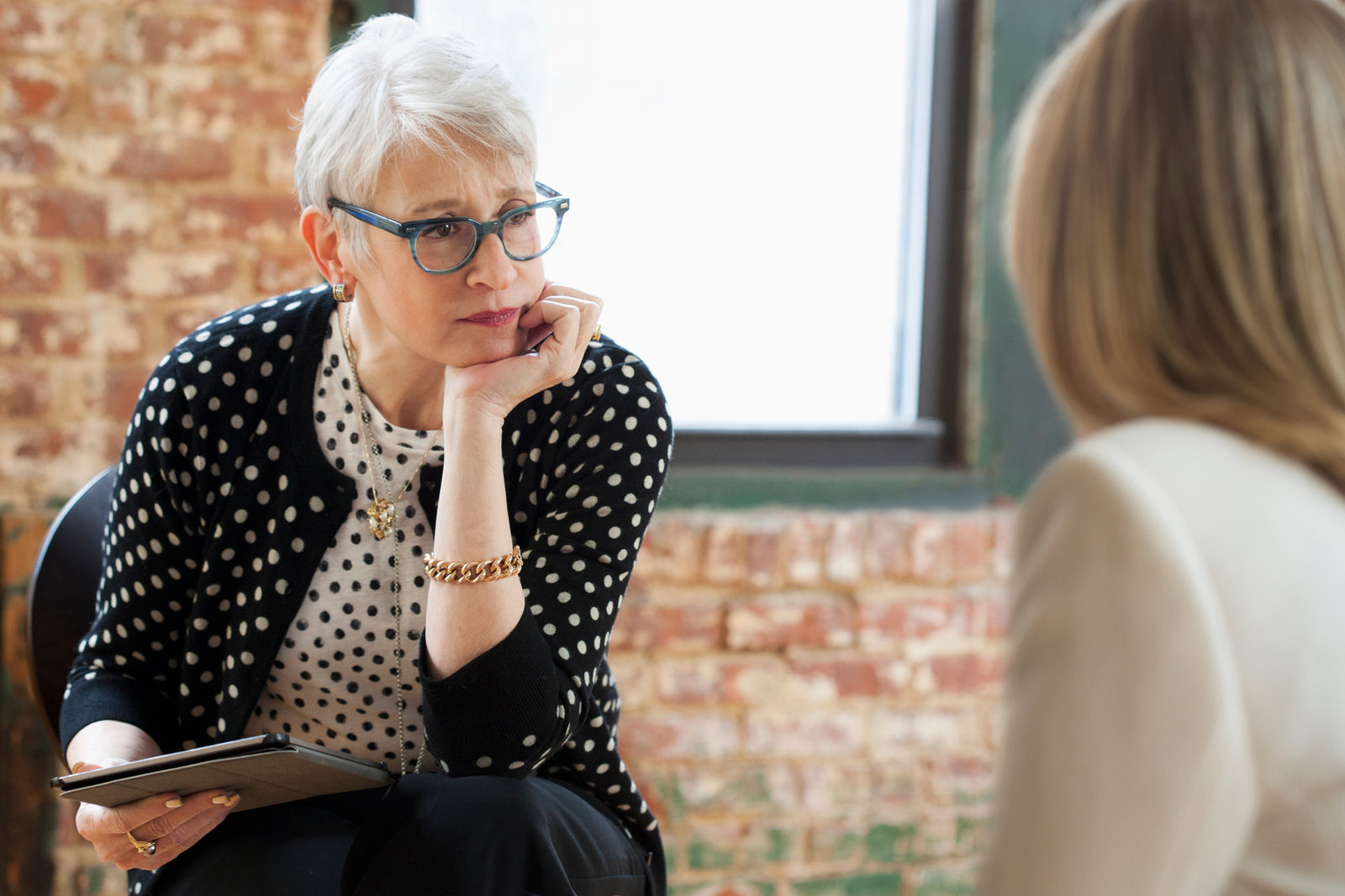 A therapist resting her chin on her hand, listening closely to a client whose back is to the camera
