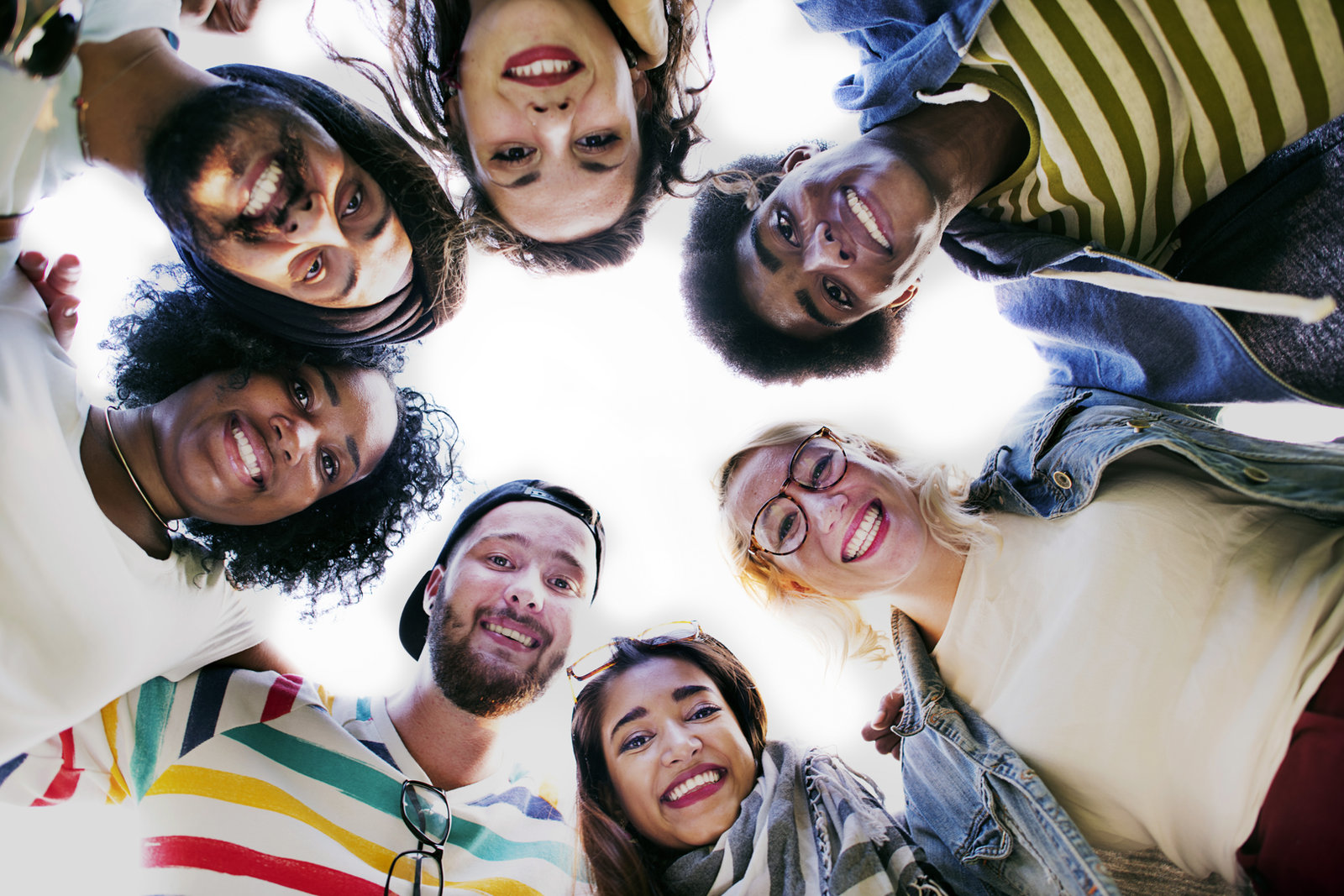 A group of colleagues standing in a circle with their heads together, looking down at the camera and smiling