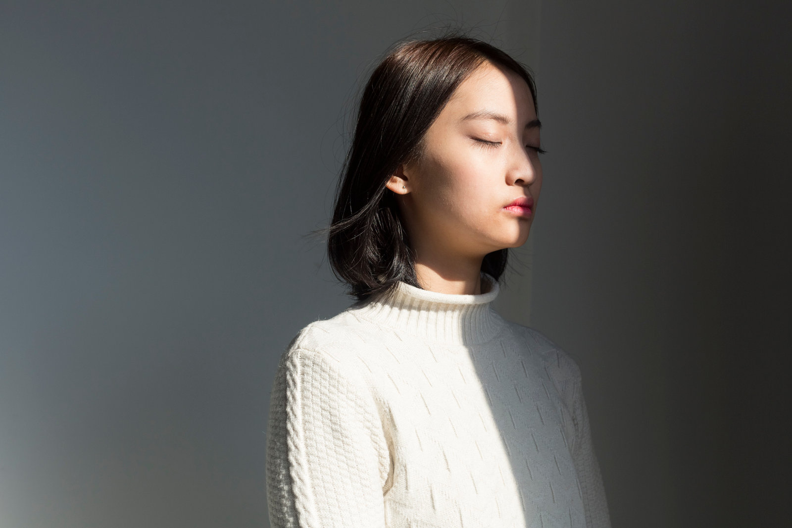 A woman standing with her eyes closed, her face lit by a shaft of sunlight