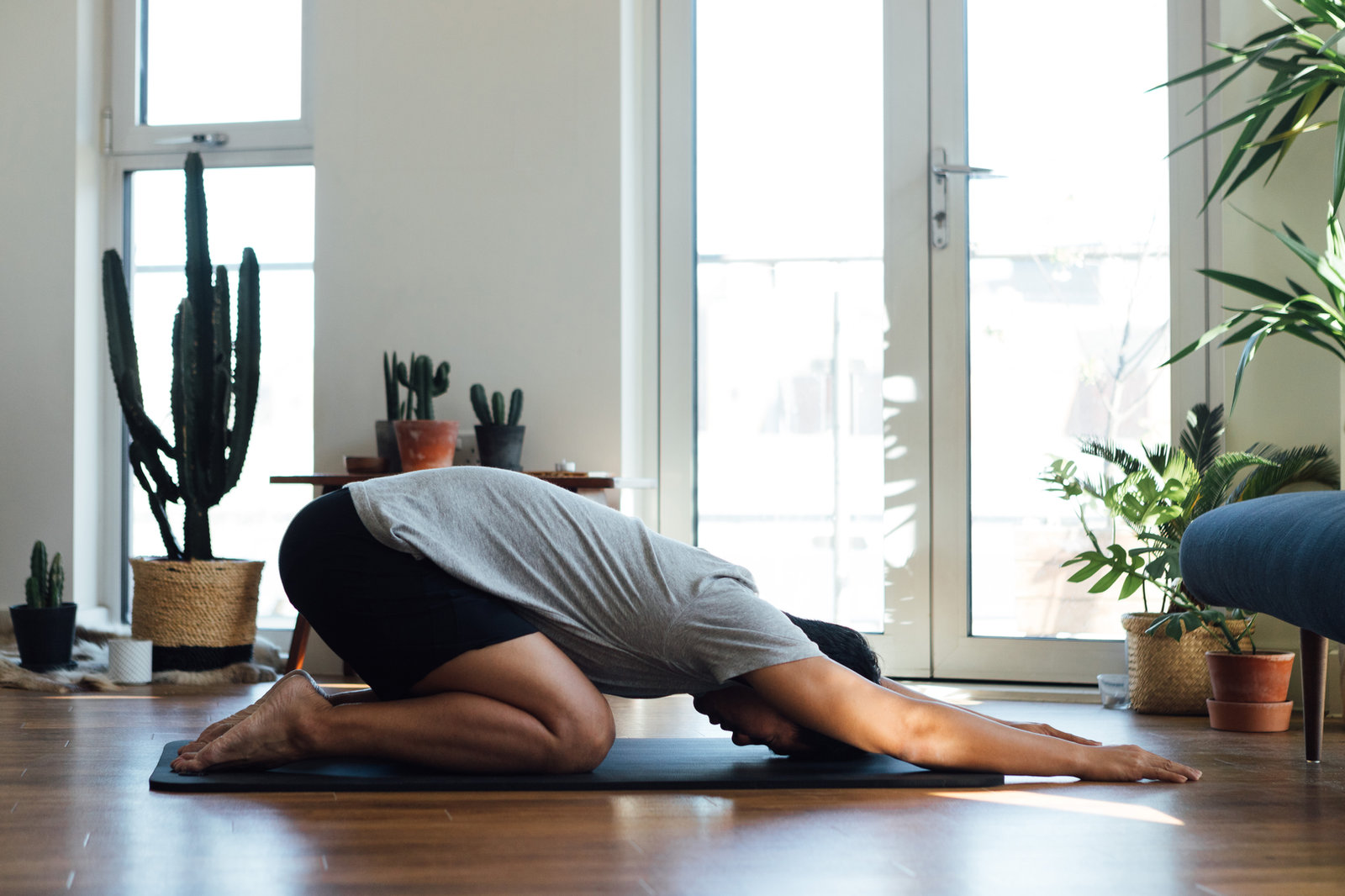 A person resting in child's pose on a yoga mat in a bright, plant-filled room