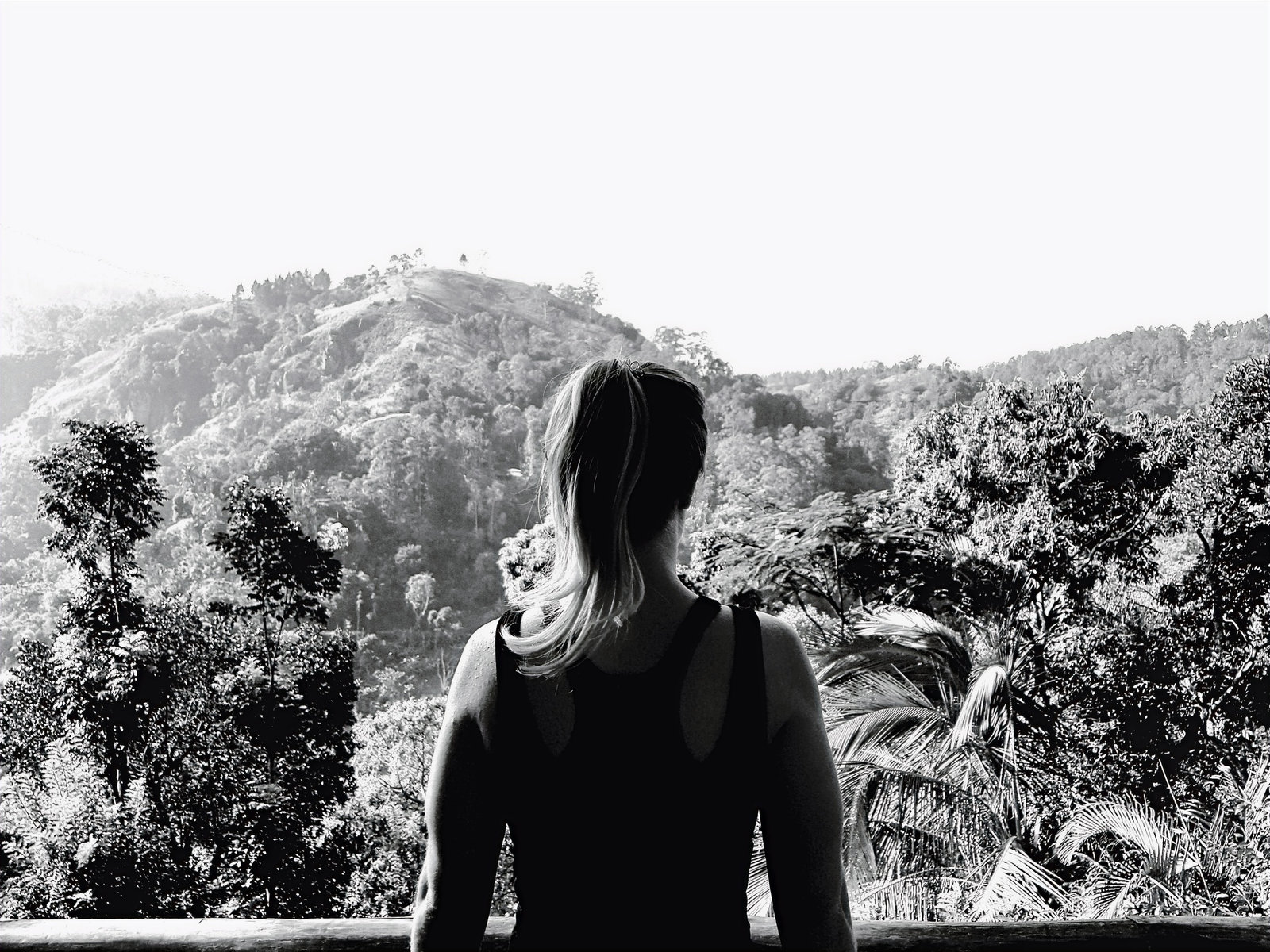 Black and white photograph of a woman seen from behind, looking out over forested hills