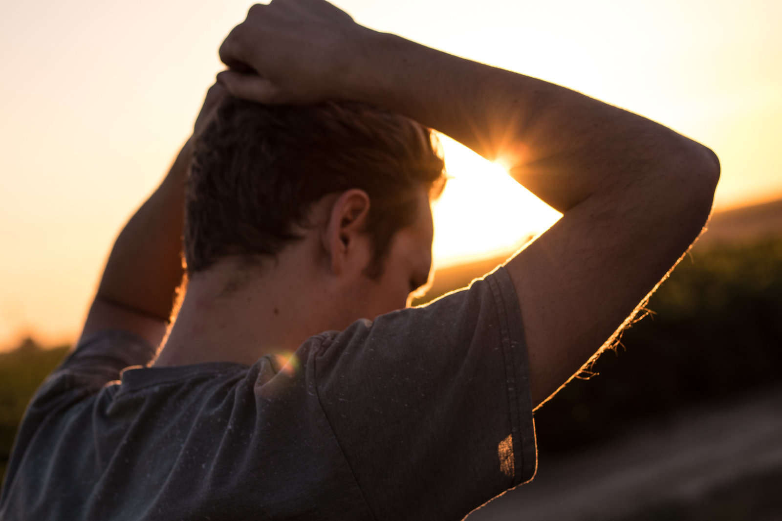 A man seen from behind with his hands behind his head, silhouetted against a low sun
