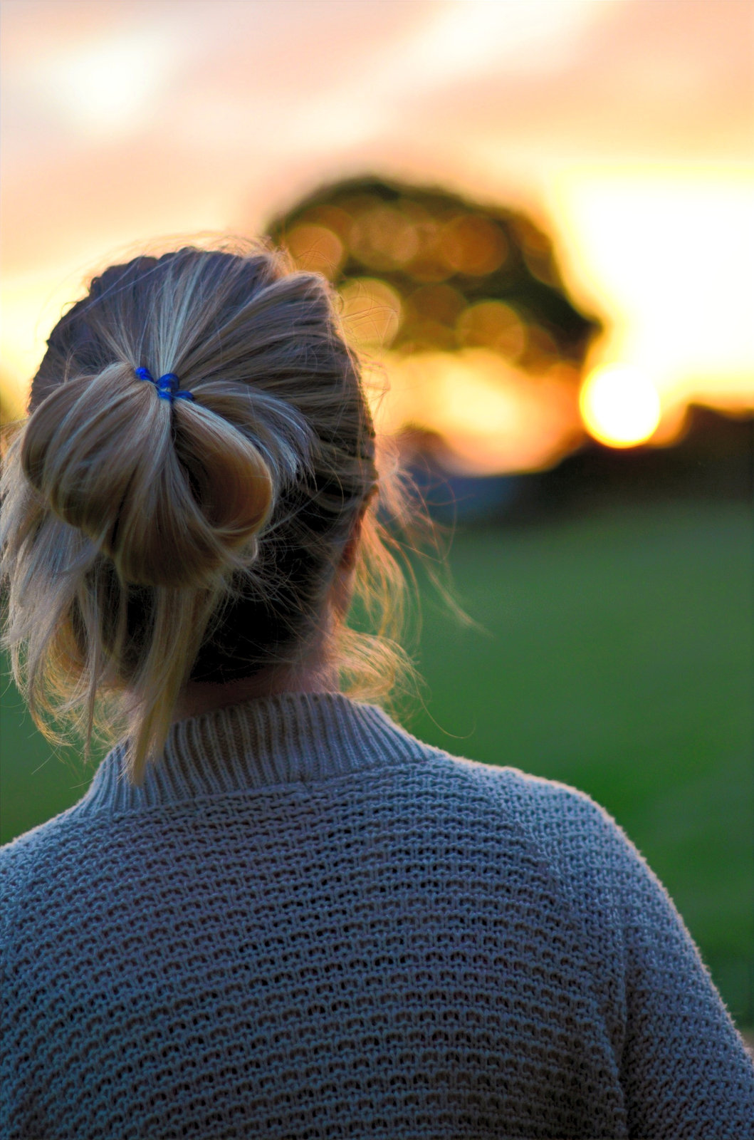 A woman seen from behind, looking out towards a sunset