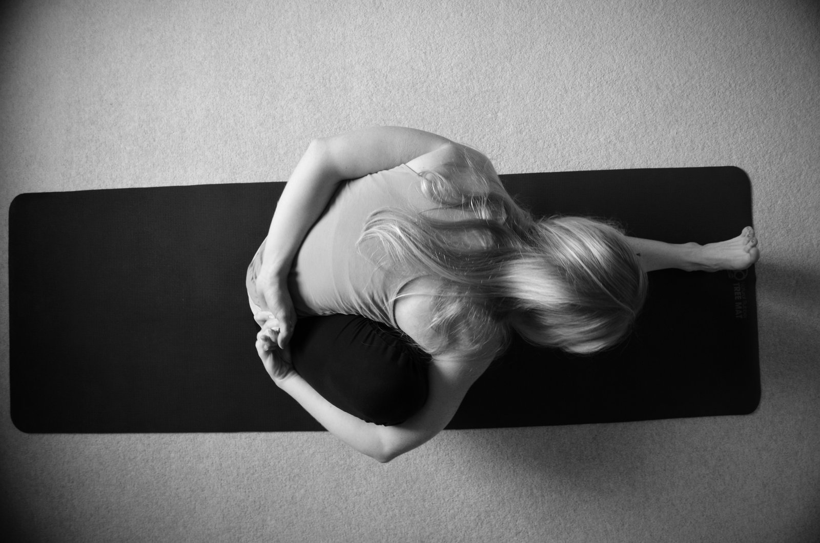 Overhead black and white photograph of a woman folding forward over one leg on a yoga mat
