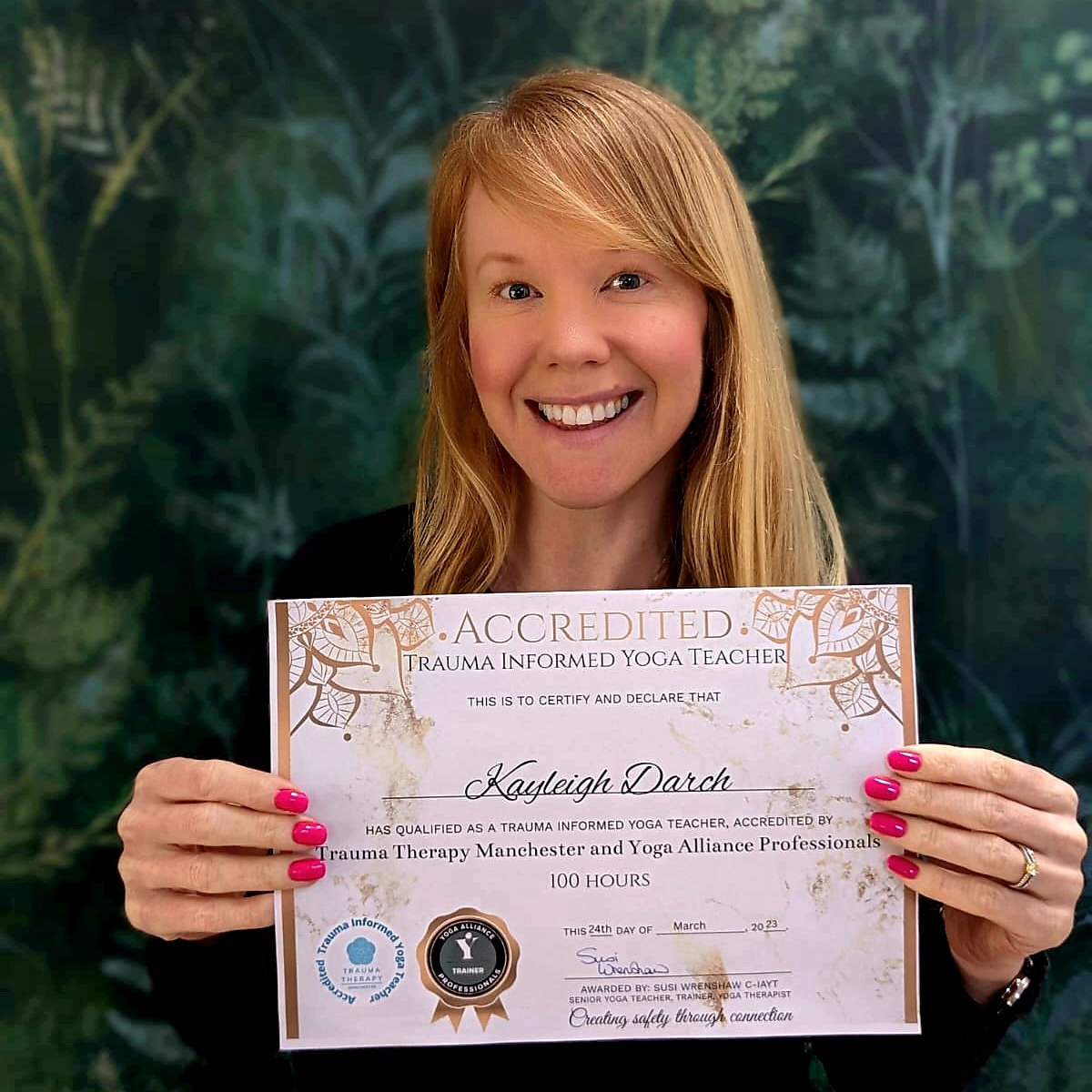 Dr Kayleigh Darch holding her accredited trauma-informed yoga teacher certificate