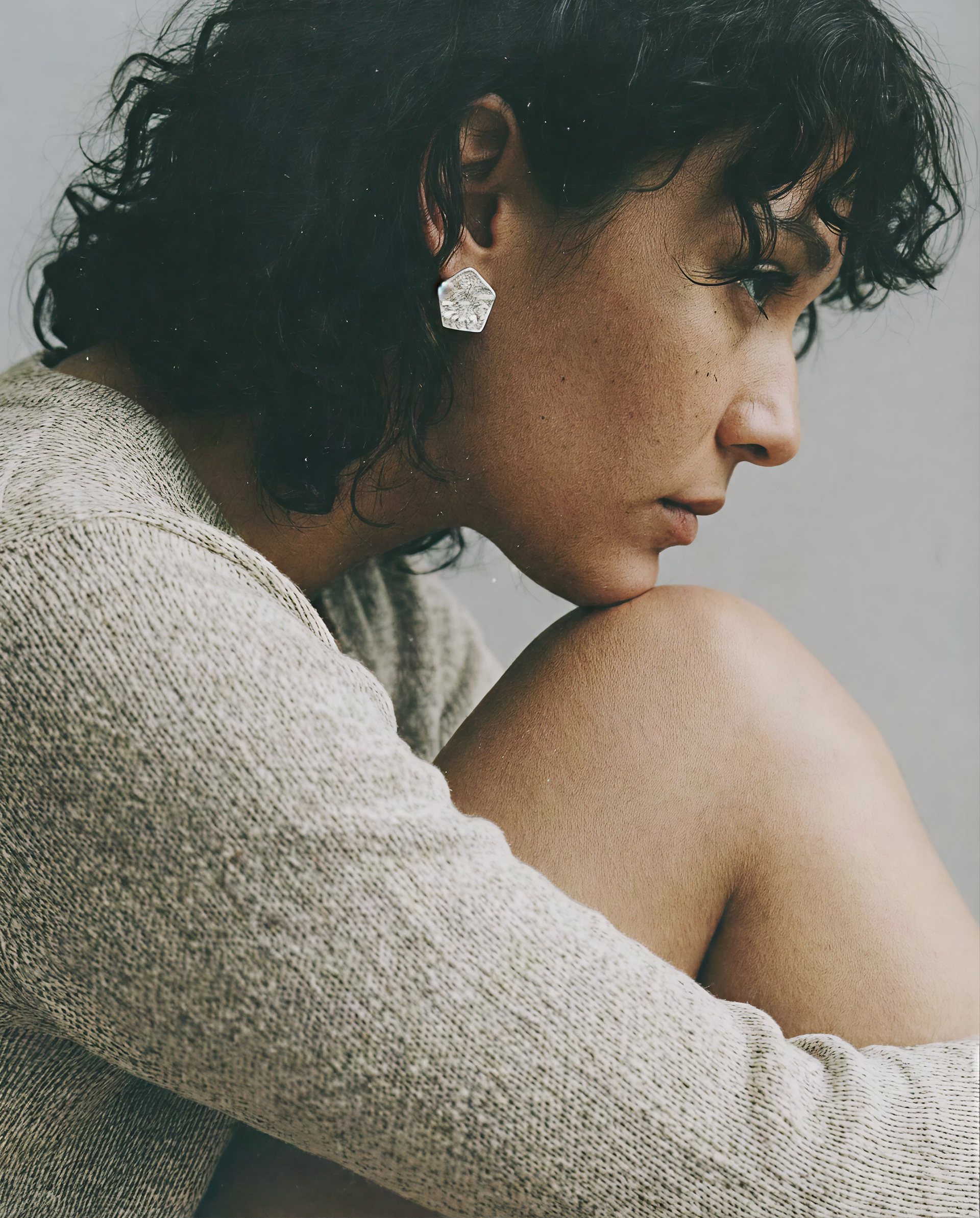 A woman in a knitted jumper resting her chin on her knee, looking away from the camera