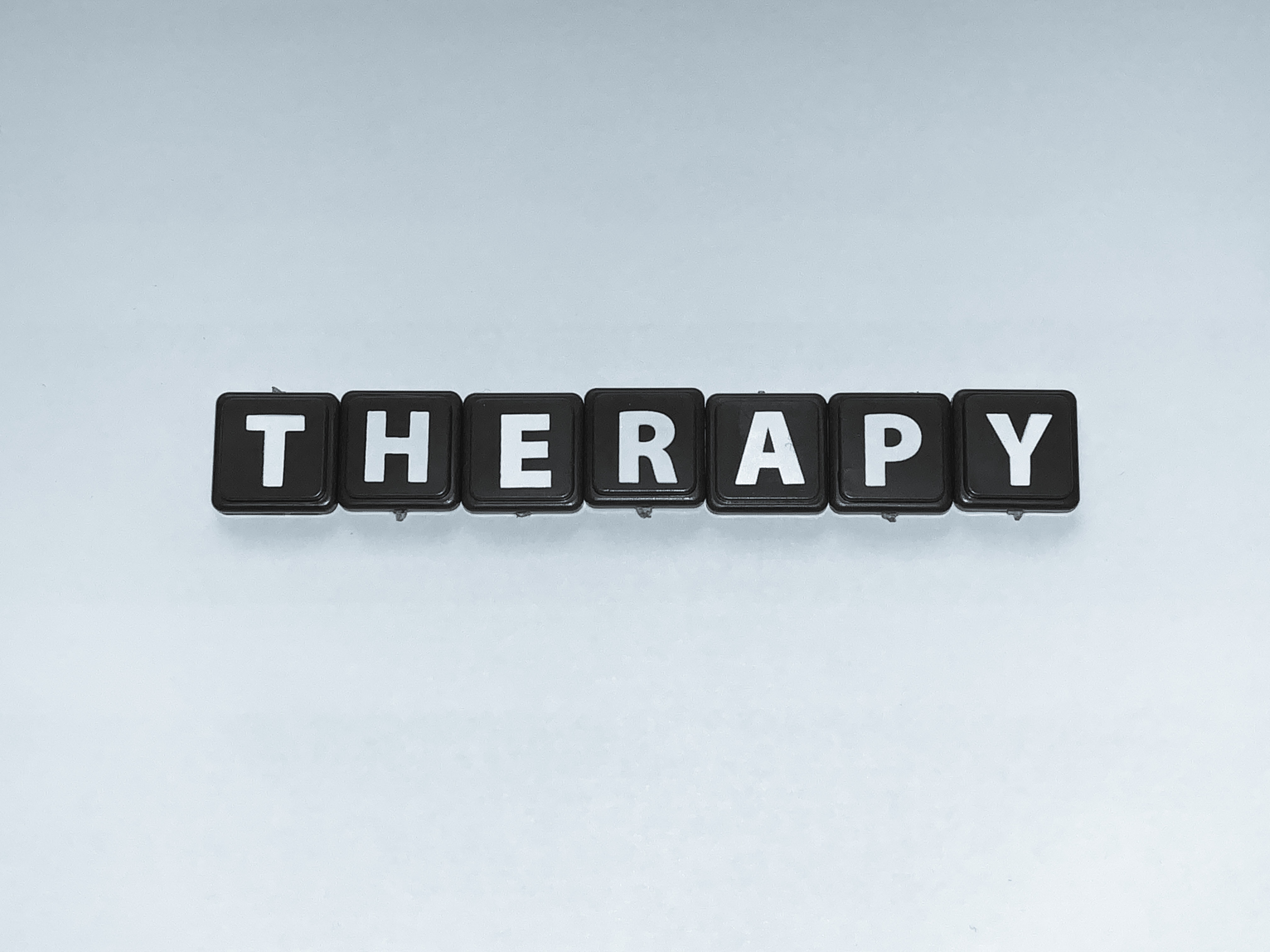Black letter tiles arranged on a pale background to spell the word therapy