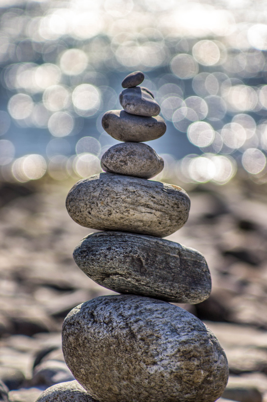 A stack of balanced pebbles on a stony beach, with sunlight glinting on the water behind