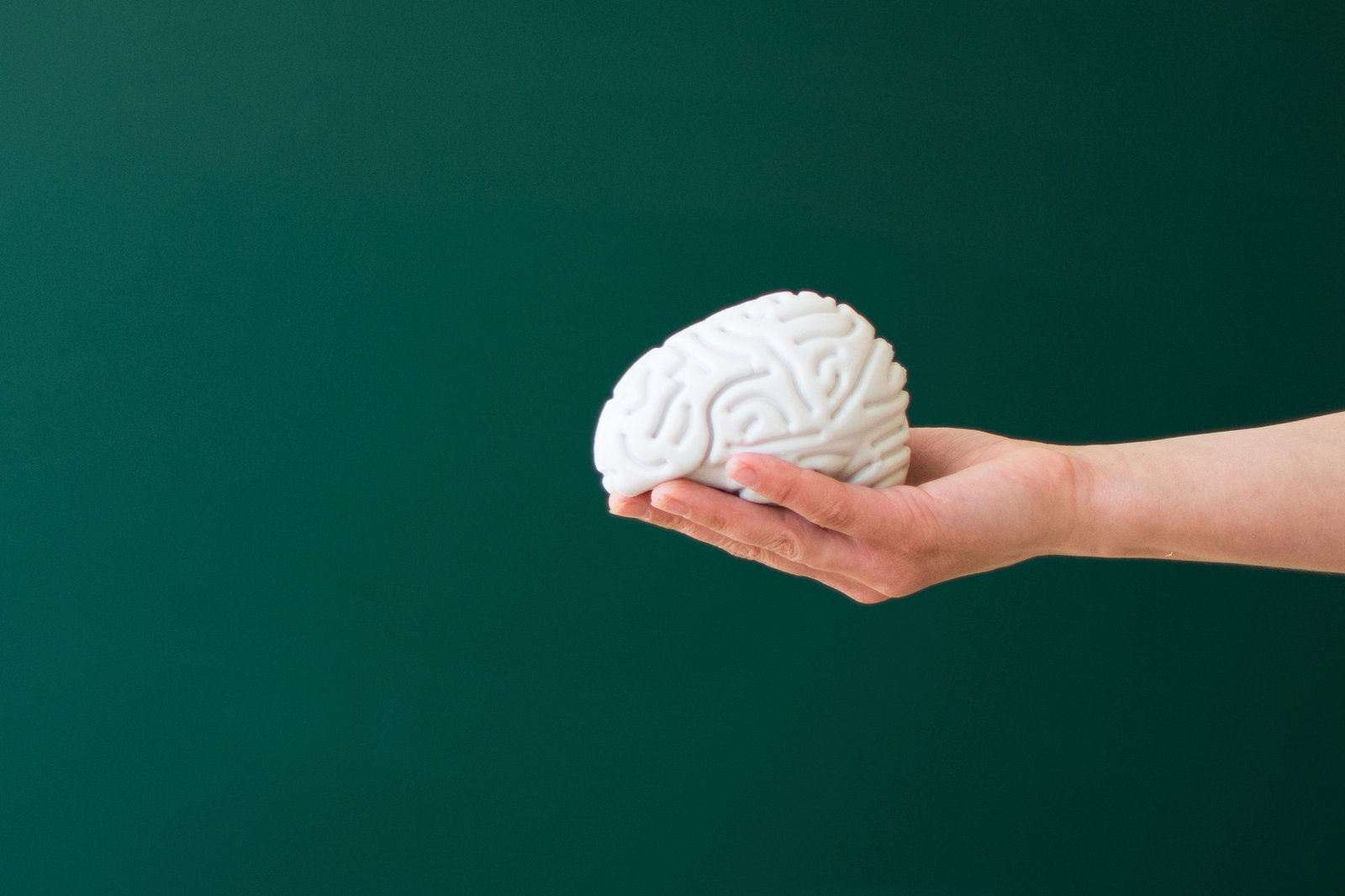 An outstretched hand holding a small model of a brain against a dark green background